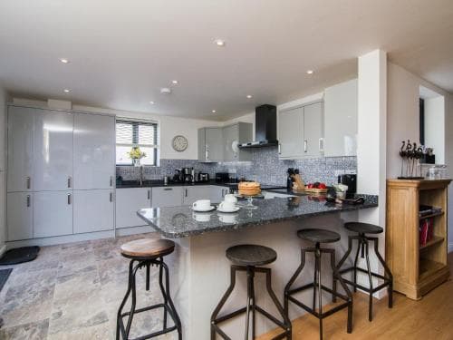 A modern kitchen with sleek white cabinets, granite countertops, and bar stools creates a cozy and inviting atmosphere, perfect for travelers seeking a comfortable self-catering accommodation.