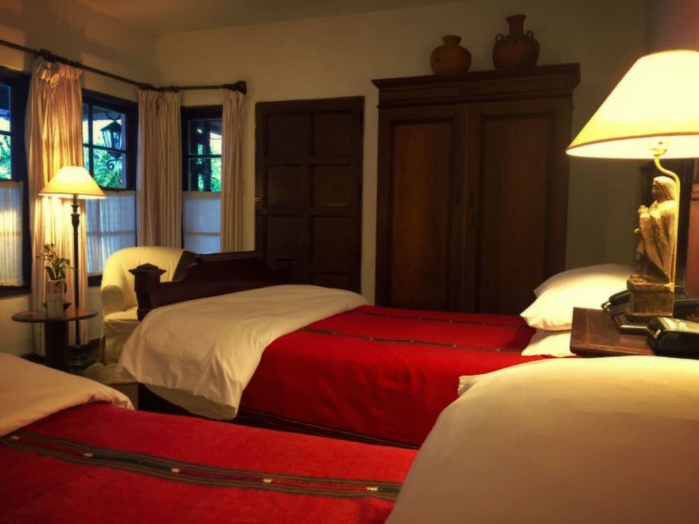A cozy hotel room with twin beds adorned in red and white linens, warm lighting from bedside lamps, wooden furnishings, and a serene view through curtained windows, ideal for travelers seeking comfort and tranquility.