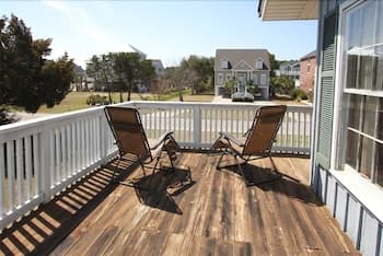 A serene suburban deck features two lounge chairs under bright sunlight, ideal for relaxing getaways or family vacations.