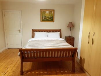 A cozy bedroom with wooden flooring, a neatly made bed, a lamp on a side table, and a wardrobe, ideal for travelers seeking a comfortable and serene accommodation experience.