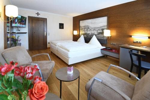 A cozy hotel room features warm wooden floors, comfortable seating, vibrant flowers, and soft lighting, creating an inviting atmosphere ideal for travelers seeking relaxation and comfort.