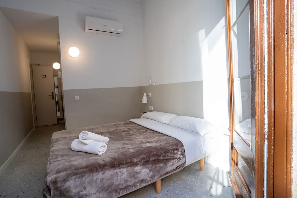 A cozy hotel room with soft lighting, neatly folded towels on the bed, and a balcony door inviting natural light, ideal for travelers seeking comfort and simplicity.