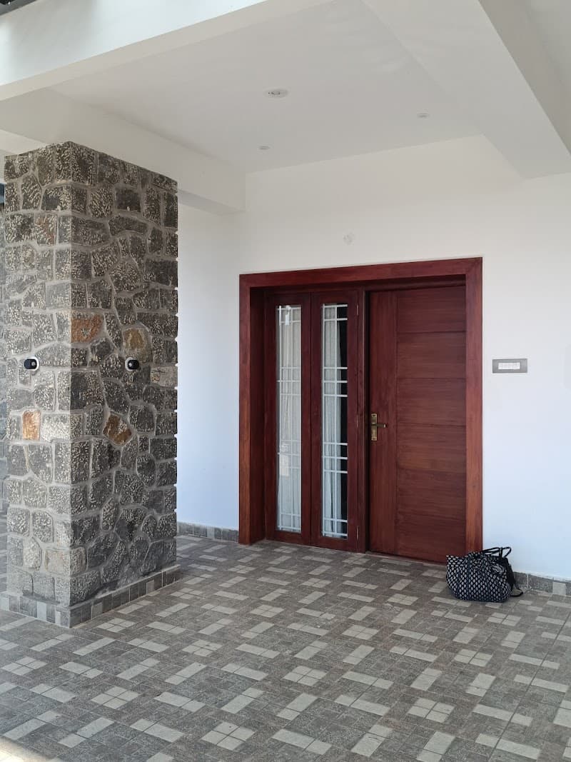 A serene entrance to a modern home in Kodaikanal, featuring a polished wooden door, stone pillar, tiled floor, and a casually placed bag, ideal for travelers seeking a cozy retreat.