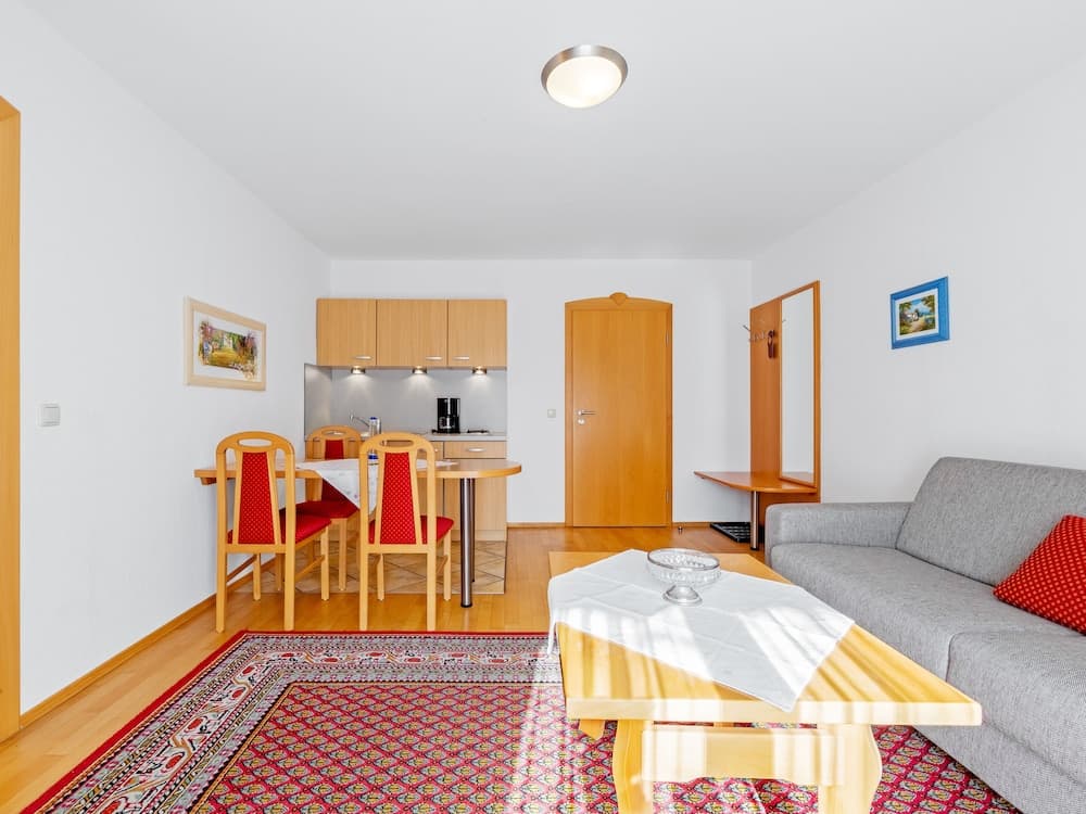 A cozy apartment interior features a warm wooden dining set, a modern kitchenette, and a comfortable living area with a gray sofa, ideal for travelers seeking a homey and functional accommodation.