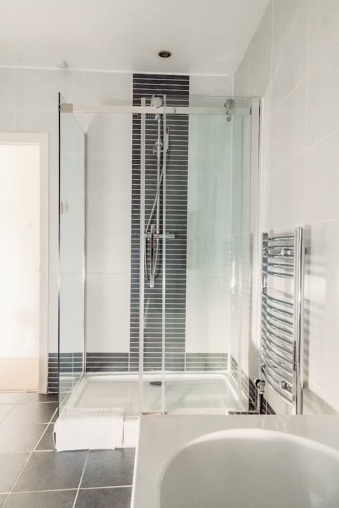 A modern bathroom features a sleek glass-enclosed shower with black accent tiles, a chrome towel warmer, and white fixtures, ideal for travelers seeking a clean and contemporary accommodation experience.