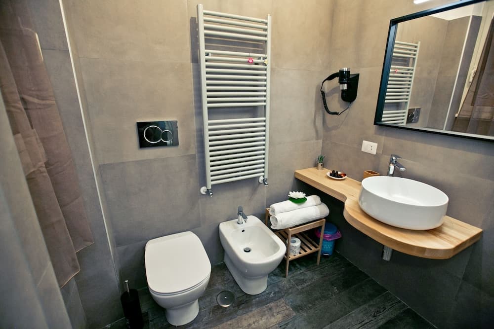 A modern bathroom with sleek gray walls, a wooden vanity, white fixtures, and a towel warmer exudes a minimalist and cozy ambiance, ideal for travelers seeking comfort in boutique accommodations.