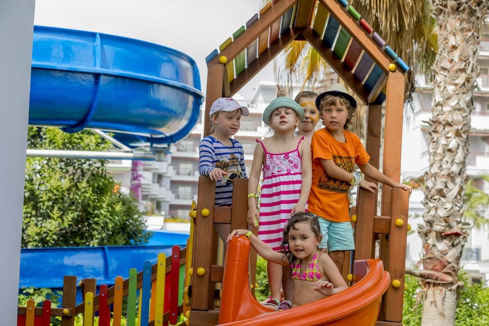 Children enjoy a vibrant playground with colorful slides and wooden structures under palm trees, creating a joyful and lively atmosphere ideal for family vacations.