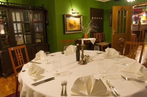 A cozy restaurant with green walls, wooden furniture, and a set dining table creates an intimate atmosphere perfect for a romantic dinner or small gathering.