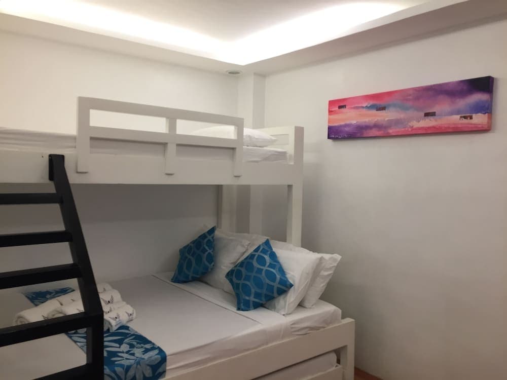 A cozy hostel room features white bunk beds adorned with blue patterned pillows and a vibrant abstract painting on the wall, ideal for budget travelers seeking comfort and style.