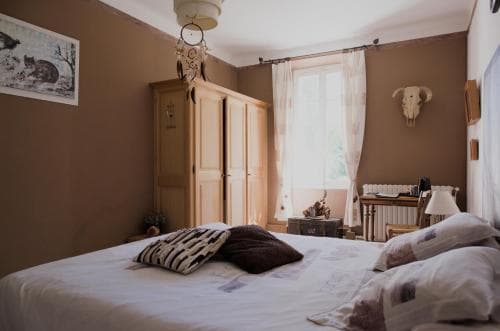 A cozy bedroom with warm brown walls, a wooden wardrobe, and soft natural light filtering through sheer curtains creates an inviting atmosphere, perfect for travelers seeking a serene and comfortable retreat.