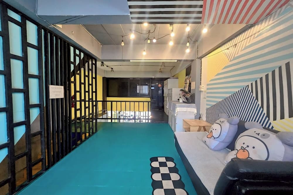 A vibrant hostel hallway features a teal floor, striped walls, cozy seating with plush pillows, and modern lighting, ideal for travelers seeking a trendy and comfortable stay.