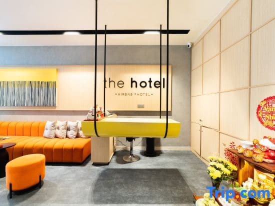A modern hotel lobby features a bright yellow reception desk, cozy orange seating, and festive decorations, creating a welcoming atmosphere ideal for travelers seeking comfort and style during their stay.