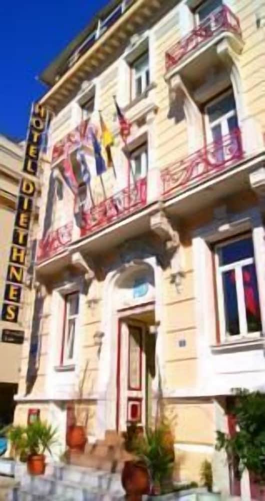 A charming European hotel facade adorned with flags and balconies under a clear blue sky, ideal for travelers seeking a cozy urban retreat.