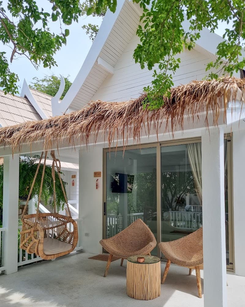 A serene tropical patio at Elephant Beach Club & Resort Samui features a thatched-roof veranda with wicker furniture and a hanging swing, perfect for relaxing under lush greenery near Chaweng Beach.
