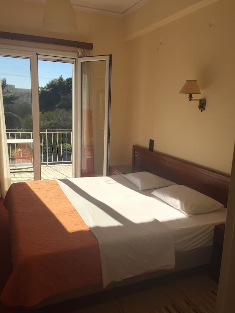 A cozy hotel room with a neatly made bed, warm lighting, and a balcony offering a serene view of greenery, ideal for travelers seeking relaxation and comfort.