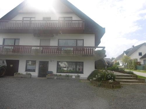 A cozy two-story house with balconies and a gravel driveway exudes a welcoming rural charm, ideal for travelers seeking a peaceful countryside retreat.