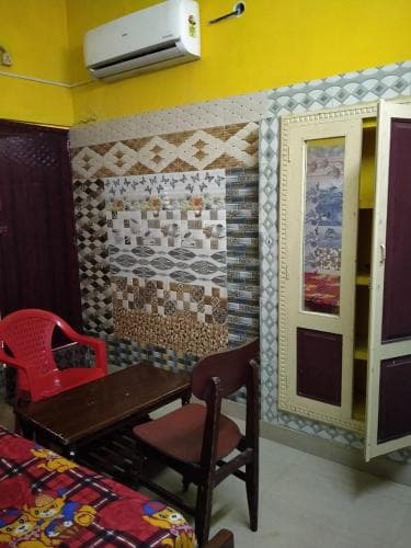 A cozy budget hotel room features vibrant yellow walls, patterned tiles, a wooden desk with chairs, a red plastic chair, and a colorful bedspread, ideal for travelers seeking affordable accommodations.