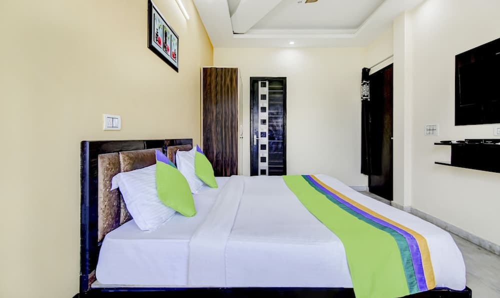A cozy hotel room features a neatly made bed with vibrant green accents, modern decor, and a mounted TV, ideal for travelers seeking comfort and convenience.