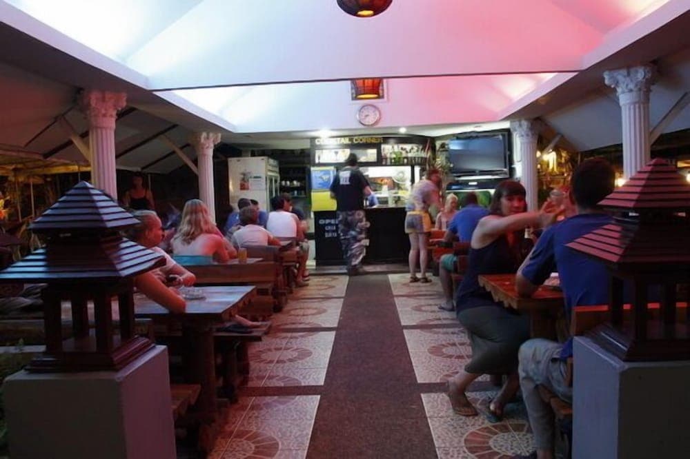 A lively outdoor dining area under a covered patio features patrons enjoying meals at wooden tables, surrounded by decorative lanterns and columns, ideal for travelers seeking a casual dining experience in a vibrant atmosphere.