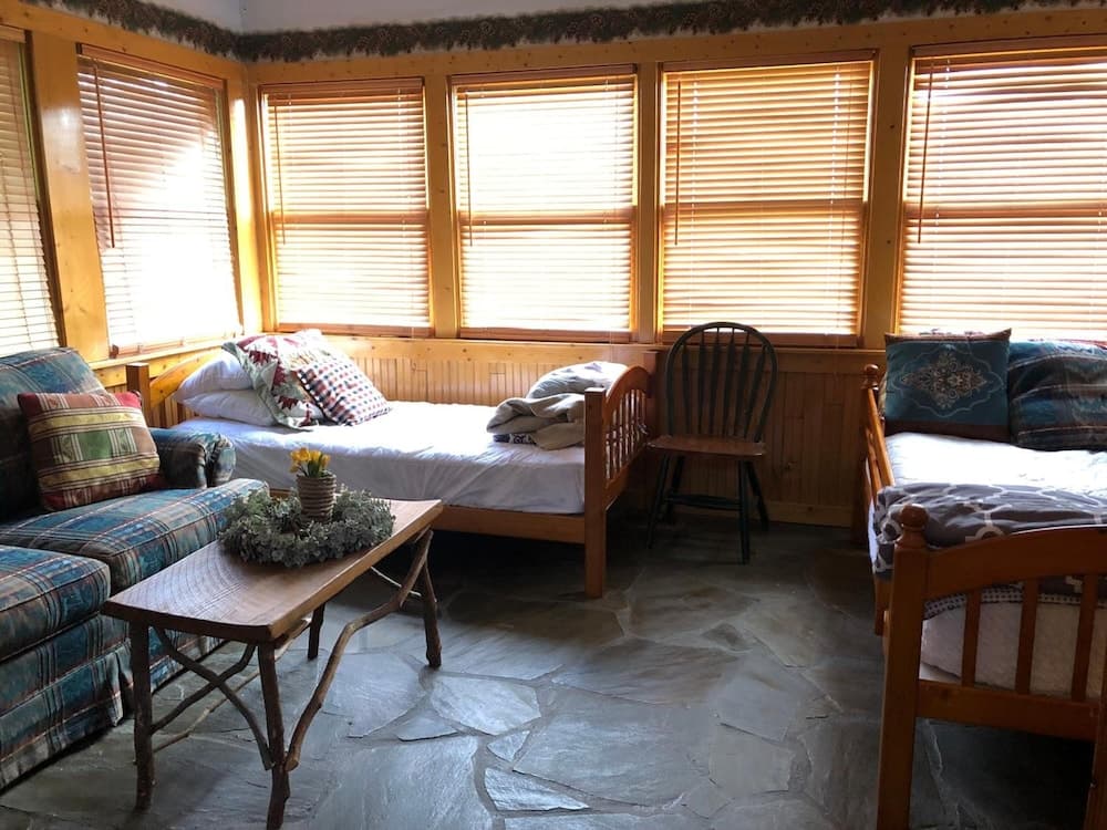 A cozy cabin interior with wooden beds, a stone floor, and large windows with blinds creates a serene retreat perfect for a relaxing getaway.