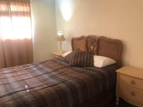 A cozy bedroom with a wooden bed adorned in earthy-toned bedding, a bedside lamp casting warm light, and sheer curtains filtering sunlight, ideal for travelers seeking a comfortable and tranquil accommodation.