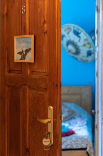 A cozy bedroom with a rustic wooden door adorned with a key and framed artwork invites travelers to relax in its vibrant blue walls and floral-patterned bedding.