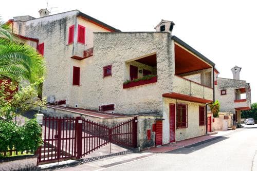 A charming Mediterranean-style residential street features pastel buildings with red accents, lush greenery, and a gated entrance, ideal for travelers seeking a quaint and peaceful neighborhood experience.