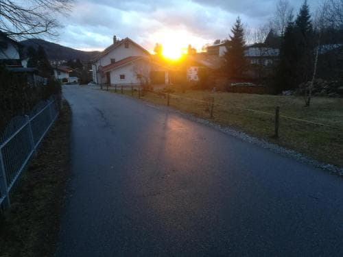 A serene suburban road at sunset glows warmly under the golden sky, framed by quaint houses, lush greenery, and distant hills, ideal for a peaceful evening stroll or photography adventure.