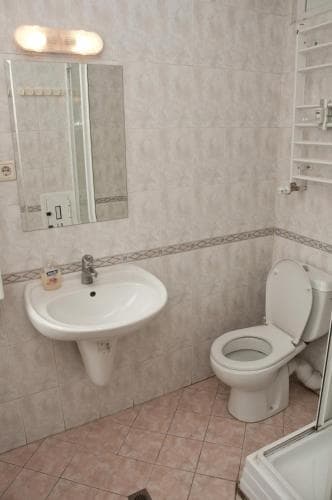 A clean, functional bathroom with tiled walls, a sink, toilet, mirror, and towel rack offers a practical space for travelers needing basic amenities.