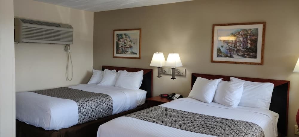 A cozy motel room features two neatly made beds with patterned throws, framed artwork on the walls, and bedside lamps, creating a welcoming atmosphere ideal for travelers seeking comfort and relaxation.