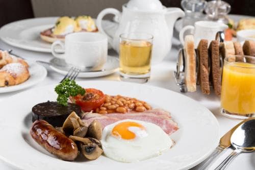 A hearty breakfast spread featuring eggs, sausages, beans, and toast on a white plate, set in a cozy dining room with a warm and inviting atmosphere, perfect for travelers seeking a comforting start to their day.