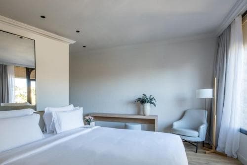 A serene hotel room features a cozy bed, modern furnishings, and soft natural light filtering through sheer curtains, ideal for travelers seeking relaxation and comfort.