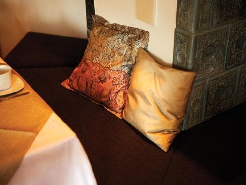 A cozy corner in a boutique hotel features plush cushions on a dark sofa beside an ornate tiled wall, creating a warm and inviting atmosphere perfect for relaxation during a travel getaway.