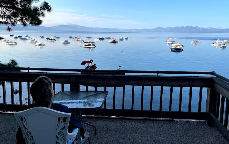 A serene lakeside deck offers a tranquil view of calm waters dotted with boats under a clear sky, perfect for a relaxing holiday retreat.
