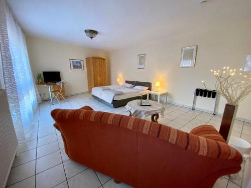 A cozy hotel room features a comfortable bed, vibrant red sofa, and modern furnishings, creating a welcoming atmosphere ideal for travelers seeking relaxation and convenience.