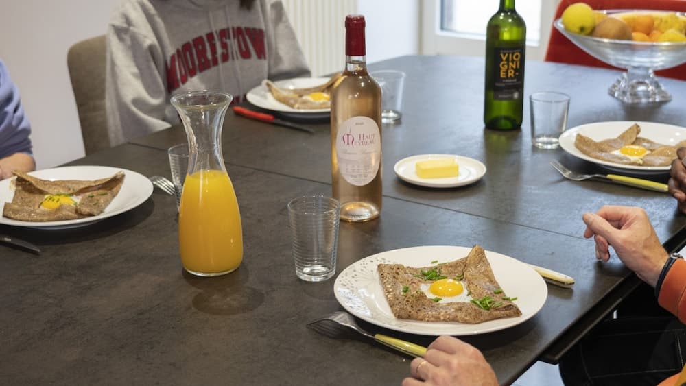 A cozy dining table scene features plates of buckwheat crepes topped with eggs, accompanied by bottles of wine and orange juice, creating an inviting atmosphere for a leisurely brunch or breakfast gathering.