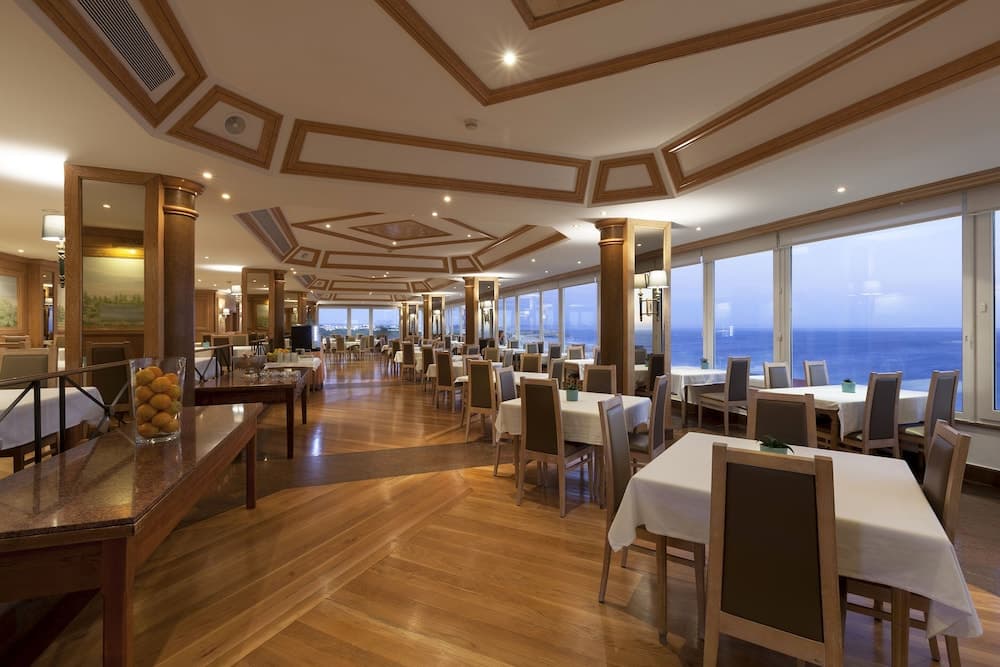 A spacious, elegant restaurant with wooden accents and large windows overlooking the ocean offers a serene dining experience, ideal for travelers seeking upscale seaside cuisine.
