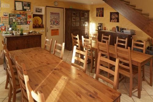 A cozy, sunlit dining area with wooden tables and chairs invites travelers to enjoy communal meals in a warm, rustic setting perfect for group retreats or family gatherings.