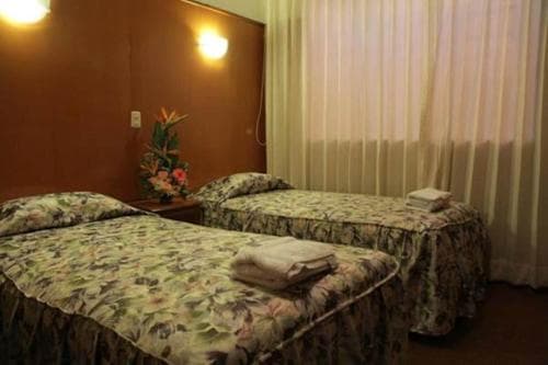 A cozy hotel room features two floral-patterned beds under warm wall lights, with a tropical flower arrangement adding charm, ideal for travelers seeking comfort and relaxation.