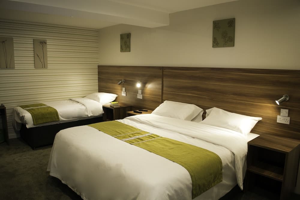 A cozy hotel room features two neatly made beds with green accents, wooden headboards, and ambient lighting, ideal for travelers seeking comfort and relaxation.