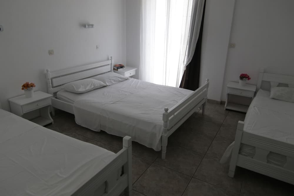 A serene hotel room with three white beds, tiled floors, and soft natural light filtering through sheer curtains, ideal for travelers seeking a clean and tranquil accommodation.
