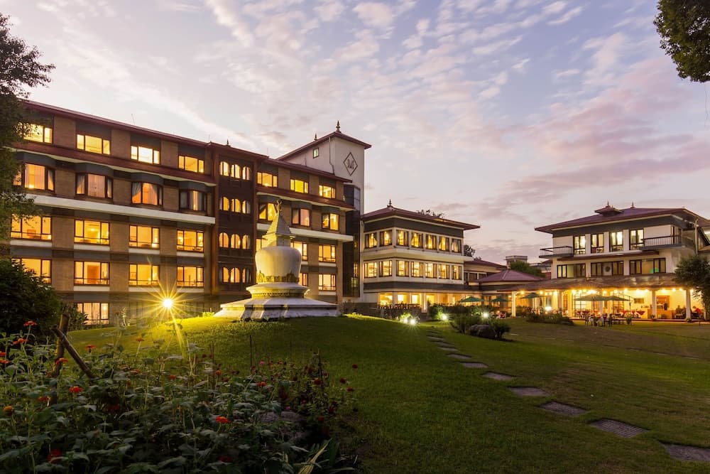 A serene evening view of a well-lit resort complex featuring traditional architecture, a central stupa, lush greenery, and warm ambient lighting, ideal for travelers seeking cultural immersion and relaxation.