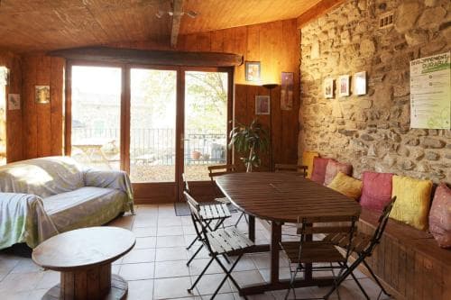 A cozy rustic living room with wooden ceilings, stone walls, and comfortable seating invites travelers to relax and enjoy the serene outdoor view through large glass doors, perfect for a tranquil getaway.