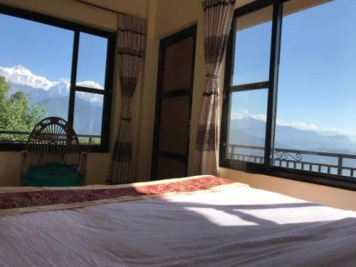 A cozy bedroom with a vibrant bedspread overlooks majestic snow-capped mountains through large windows, ideal for travelers seeking serene mountain retreats.