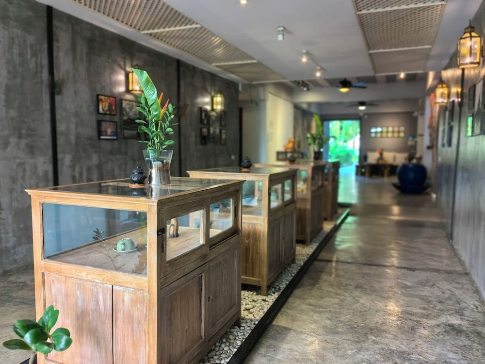 A serene indoor gallery space features rustic wooden display cabinets adorned with greenery and small artifacts, set against a backdrop of concrete walls and warm lighting, ideal for travelers seeking cultural and artistic experiences.