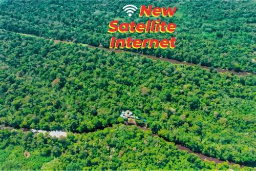 An aerial view of a lush tropical forest with a small settlement nestled among the greenery, promoting new satellite internet connectivity, ideal for travelers seeking remote adventure with modern amenities.