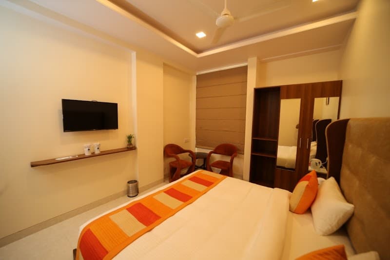 A cozy hotel room at Hotel Myriad Inn in Jaipur, Rajasthan, features warm lighting, a neatly made bed with orange accents, a mounted TV, and comfortable seating, ideal for travelers seeking relaxation and convenience.