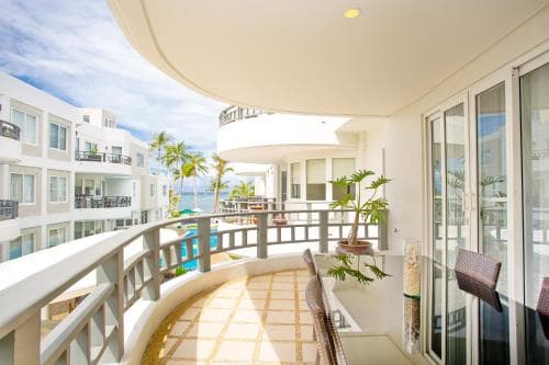A serene balcony with modern furnishings overlooks a tropical beachfront property, ideal for vacationers seeking relaxation and scenic views.