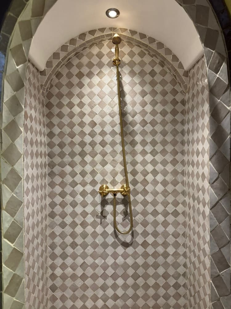 A luxurious shower with gold fixtures and diamond-patterned tiles creates an elegant ambiance ideal for high-end hotel or spa experiences.