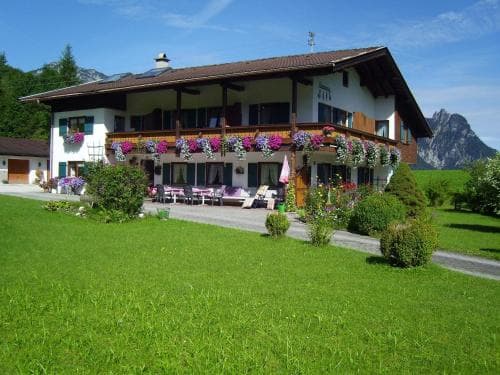 A charming alpine guesthouse adorned with vibrant flower boxes sits invitingly amidst lush greenery and towering mountains, perfect for travelers seeking a serene and picturesque retreat.